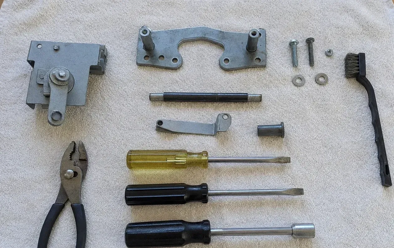 Oven door hinge assemblies, a hinge plate and roller pins laid on a towel beside a wire brush, pliers and screwdrivers